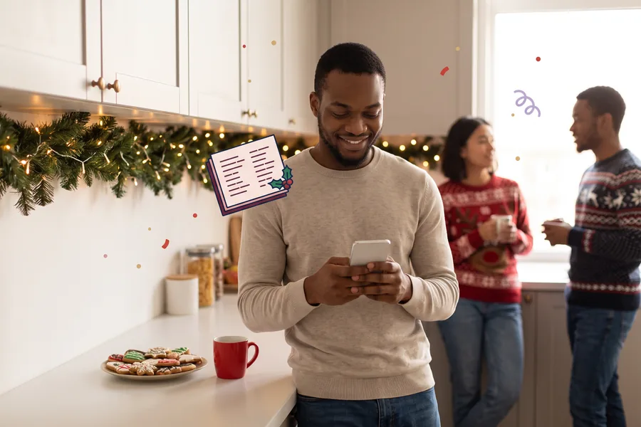 Man scrolling his phone at an office kitchen counter decorated with garland and Christmas cookies