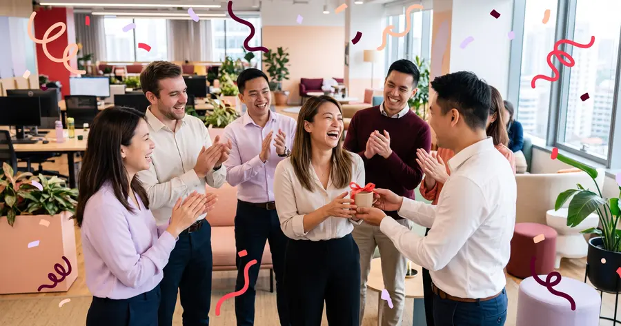 Teammates applauding a laughing employee at a morning stand-up as one hands her a coffee with a ribbon