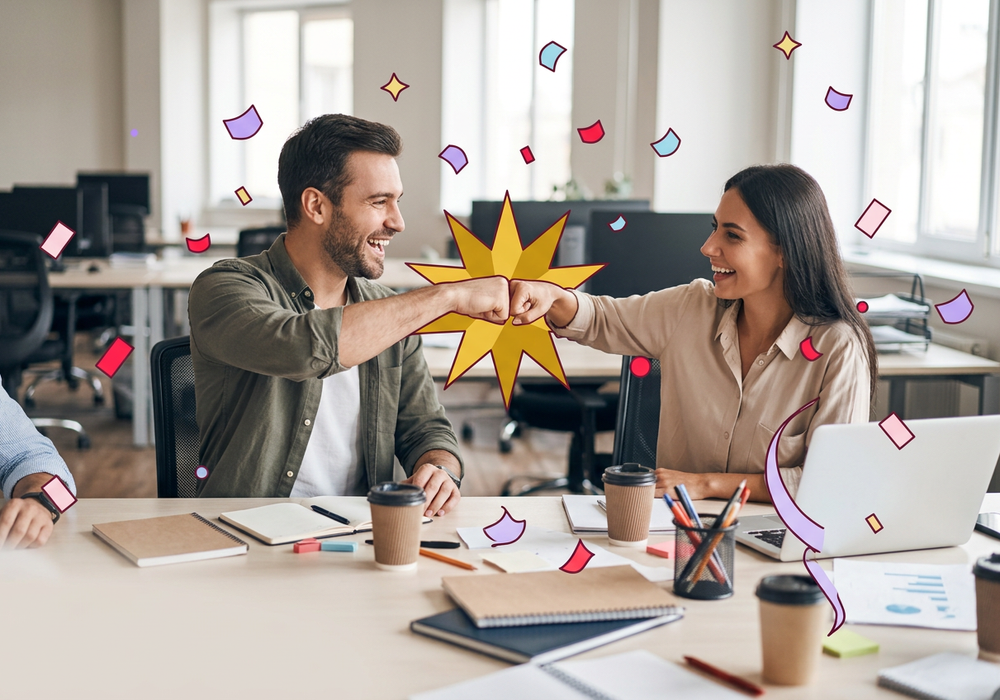 Two colleagues fist-bumping at a desk with an illustrated gold starburst at the point of contact